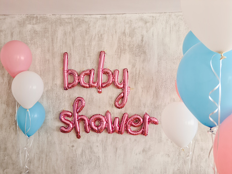 Pink baby shower balloon sign on the wall indoors.