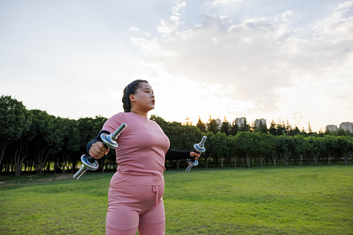A young asian woman, obese. She uses dumbbells to exercise outdoors, confidently changing her body.