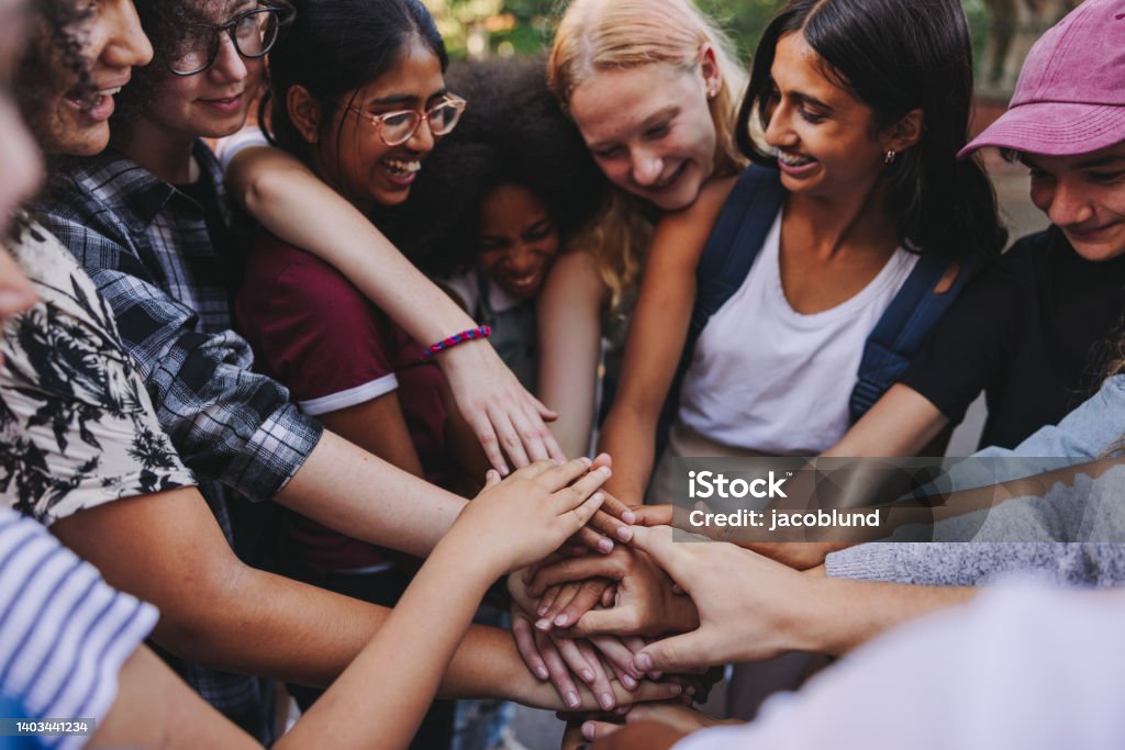 Cheerful teenagers putting their hands together in unity Diverse teenagers smiling cheerfully while putting their hands together in a huddle. Group of generation z youngsters symbolizing team spirit and togetherness. Community Outreach Stock Photo