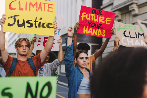 Young people marching against climate change and global warming. Multicultural climate activists protesting with posters and banners. Group of teenagers joining the global climate strike.