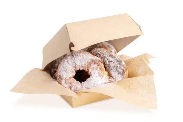 Fresh delicious homemade doughnuts sprinkled with powdered sugar on kraft napkins in a slightly open box isolated on white. Donuts. Delivery service and sale in a sweet pastry shop, confectionery.