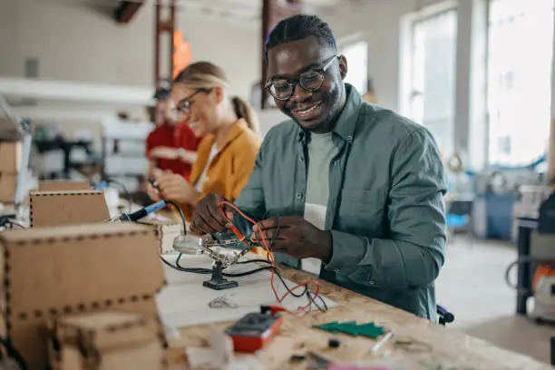 Ona male african American and one Caucasian female student working in the tech center. He is checking the electricity current of the circuit board