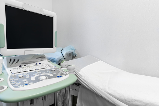 Doctor's office with couch and diagnosis tools. Close-up of ultrasound machine in clinic. Modern hospital with high technology equipment. Health care, diagnostic and disease prevention concept.