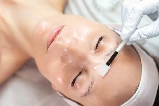 Photo of Close-up beautician doctor hand making anti-age procedure apply peeling acid young attractive female client at beauty clinic. Cosmetologist specialist doing skincare treatment. Health care therapy