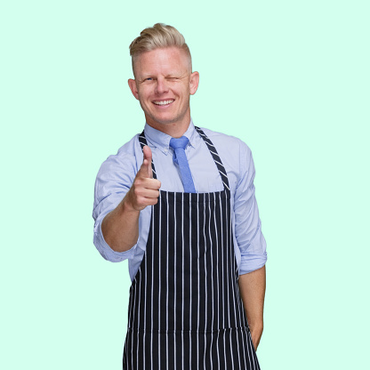 Waist up of aged 30-39 years old with blond hair caucasian male butcher standing in front of black background wearing button down shirt who is smiling and showing finger gun who is pointing
