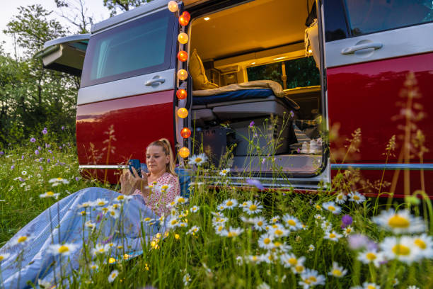 istock Woman using smart phone amidst plants while resting against illuminated campervan 1403454686