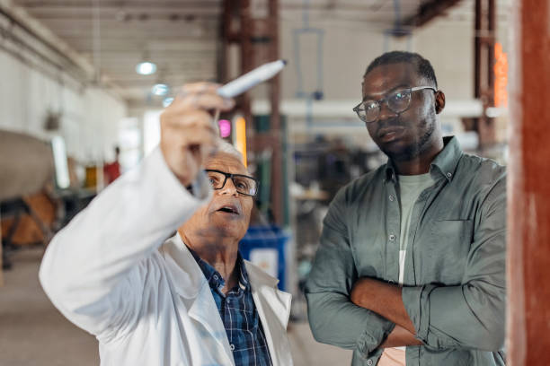 Trying to find a solution An older Caucasian man and a younger African American man are looking at an equation on a transparent writing board. transparent wipe board stock pictures, royalty-free photos & images