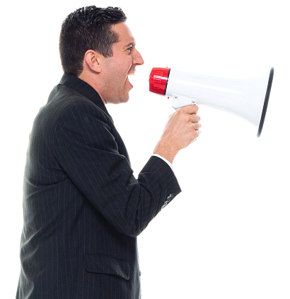Portrait of caucasian young male business person standing in front of white background wearing businesswear who is serious and holding megaphone