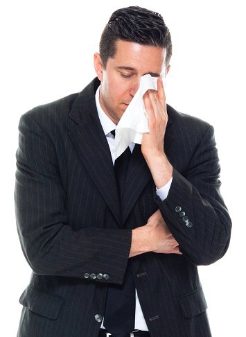 Front view of caucasian male manager standing in front of white background wearing businesswear who is crying and holding facial tissue