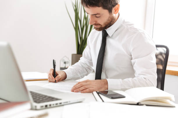 istock Image of concentrated office worker 30s wearing white shirt working with laptop and notebook, in modern workplace 1403459340
