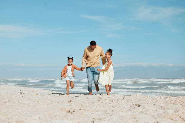 istock Cheerful young mixed race father running on the beach with his two daughters. Two energetic little girls enjoying day at the beach while on holiday with their dad 1403459427