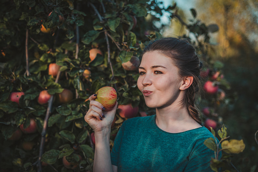 Young woman biting a red apple in the garden and enjoying the flavor of the fruit