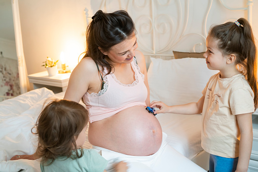 Smiling pregnant woman  with her daughter's playing with cars on he belly