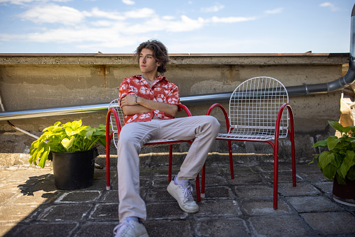 Portrait of teenage gay male person, sitting on the chair on the rooftop