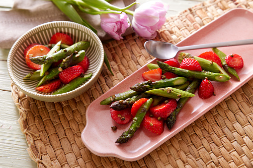 From above of delicious fresh salad with asparagus and strawberry served in plates on table for vegetarian lunch
