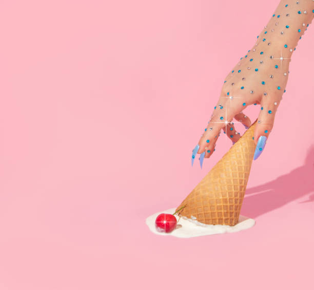 Summer creative layout with woman hand with sparkle stones reaching melting upside down ice cream cone with cherry on pastel pink background.  70s, 80s or 90s retro aesthetic fashion idea. Minimal summer romantic idea.