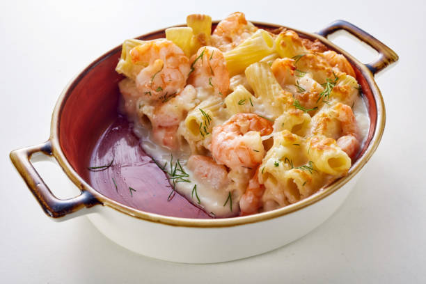 Tasty pasta with seafood baked in casserole and served on table High angle of appetizing gratin made of rigatoni pasta and shrimps baked in ceramic deep pan with creamy sauce and herbs and served on white table seafood gratin stock pictures, royalty-free photos & images