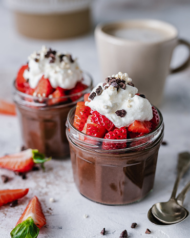 Two jars filled with chocolate mousse and topped with strawberries and cream