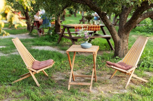 Garden furniture for leisure time in nature. Wooden chairs and table table in summer orchard. Wooden outdoor furniture set for Picnic in garden. Cozy Interior Courtyard with table and sun loungers in