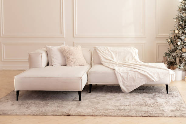 istock Elegant modern interior living room with large light  corner sofa. Comfortable couch with three cushions and a blanket standing in bright room interior with grey carpet in a modern interior. 1403468907