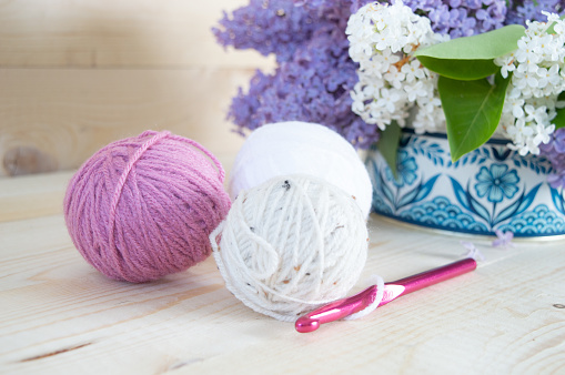 colorful woolen balls with crochet hook on wooden ground with purple lilac flower
