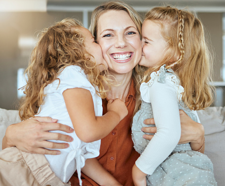 Happy young mom enjoying leisure time with daughter kid at home. Mother sitting on cozy couch, hugging girl, talking to child. Family relationship, motherhood, trust, upbringing concept