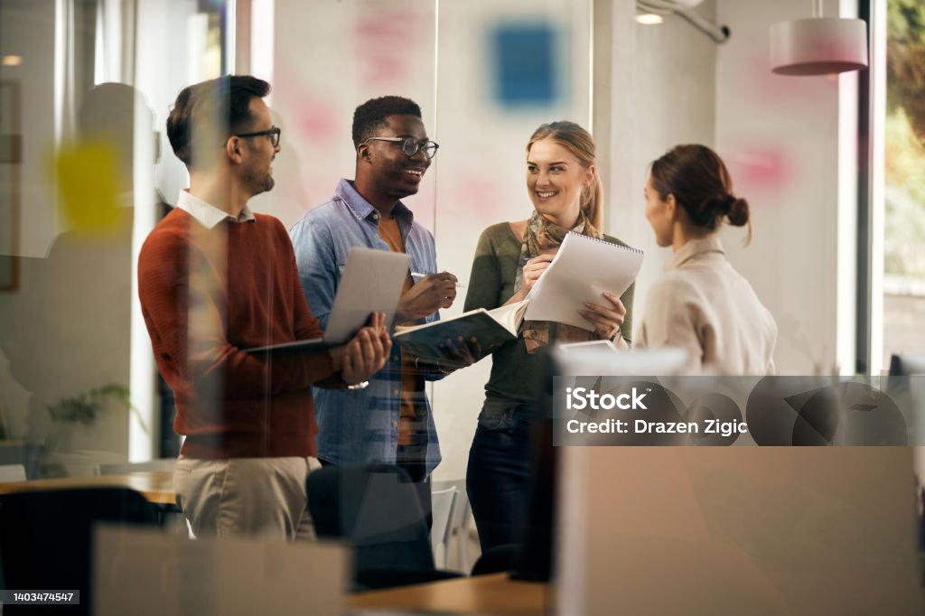 Young start-up team talking and having fun while working at creative office. Happy multiracial business team having fun while talking during a meeting in the office. Employee Engagement Stock Photo