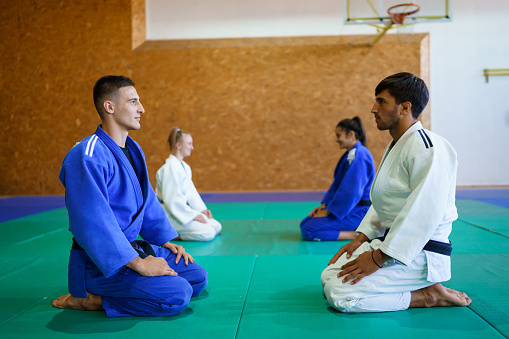 Two young couples of judo martial art partners sitting and greeting each other before fight