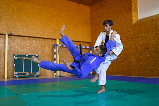 Two male judokas in a fight , one is grabbing his opponent and throwing him on the floor
