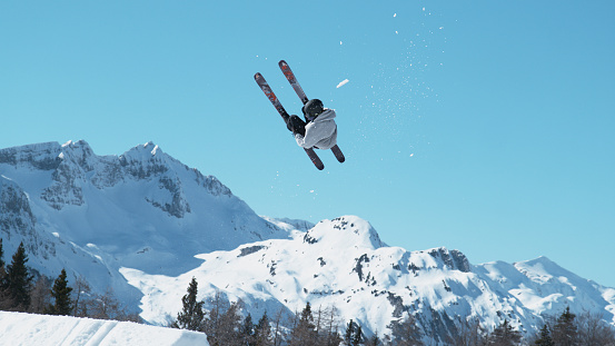 Athletic male tourist freestyle skiing in the Slovenian mountains does a flip trick on a sunny winter day. Spectacular shot of an extreme skier jumping off a kicker and doing a beautiful backflip.