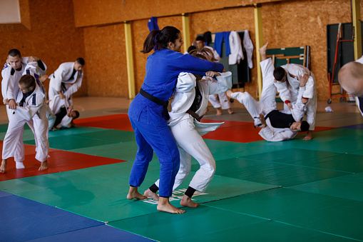 Martial arts fighters training together. Group of young male and female  judokas in white and blue martial arts clothing practicing throwing technique