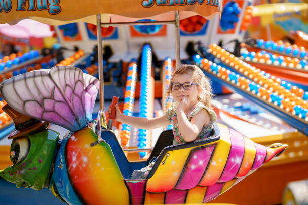 adorable little preschool girl with glasses riding on animal on roundabout carousel in amusement park. happy healthy baby child having fun outdoors on sunny day. family weekend or vacations - glasses child cute offspring imagens e fotografias de stock