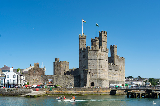 Caernarfon, United Kingdom - July 17, 2021: Toursits and locals people walk around Caernarfon castle and harbor in North Wales
