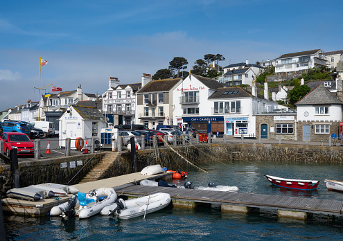 St Mawes, United Kingdom - May 18, 2022: The small harbour with moored boats and shop fronts lining the seafront town.