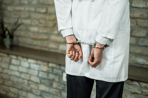 Hand close-up of unrecognizable doctor in handcuffs getting arrested.