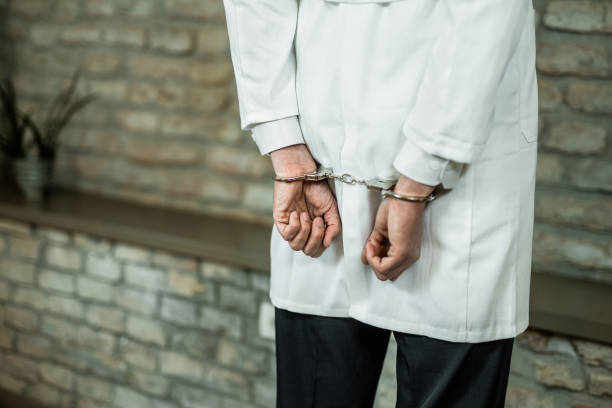 Handcuffed male doctor getting arrested. Hand close-up of unrecognizable doctor in handcuffs getting arrested. arrest photos stock pictures, royalty-free photos & images