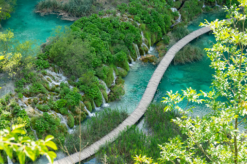 AERIAL: Drone shot of a wooden walkway crossing a gorgeous lake in a famous tourist attraction in Croatia. Scenic empty boardwalk runs past an emerald colored lake in the scenic Plitvice national park