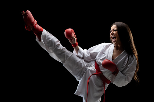 girl exercising karate leg kick and screaming against black background