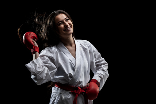 beautiful happy girl girl posing and smiling in karate outfit kimono and red gloves against black background