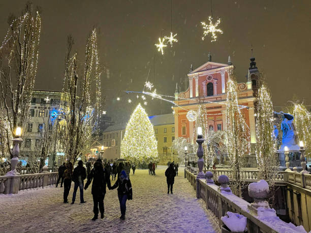 tourists walk across a bridge and towards the christmas tree in preseren square. - ljubljana december winter christmas imagens e fotografias de stock