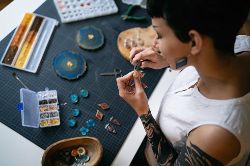 Young Caucasian woman, using pliers while making epoxy jewelry at her workshop