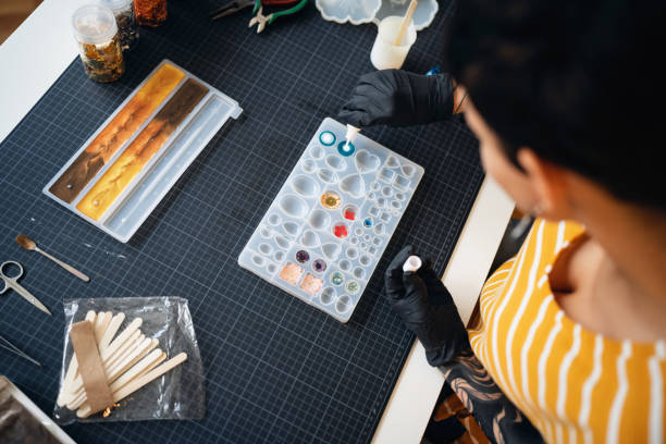 Craft woman pouring epoxy in the silicone mold, while working from her home workshop