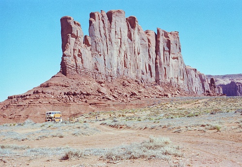 The photograph shows a giant cliff in Monument Valley and how small a large double-decker bus seems in relation to the cliff, size proportions
