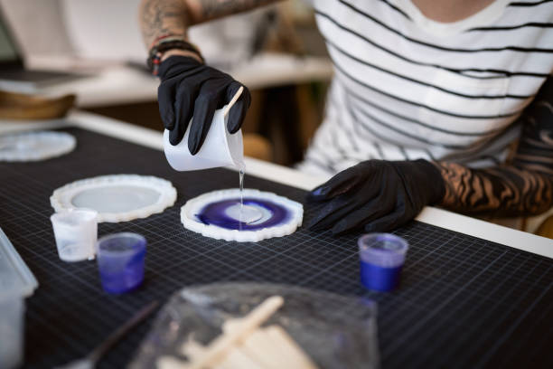 Craft woman pouring epoxy in the silicone mold, while working from her home workshop stock photo