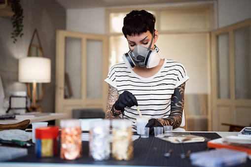 Young Caucasian woman, preparing and mixing epoxy, while working from her home workshop, while wear respirator mask
