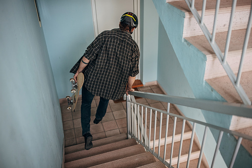 One man, male skater carrying a skateboard while walking down the steps in building.