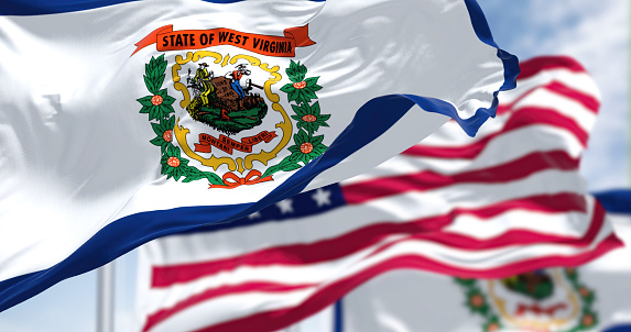 The West Virginia state flag waving along with the national flag of the United States of America. West Virginia is a state in the Southeastern region of the United States