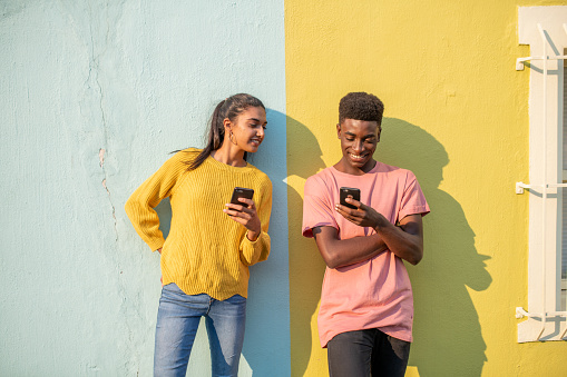 Millennials using mobile phone on light blue\\yellow wall. Girl is looking tat mobile phone of her boyfriend