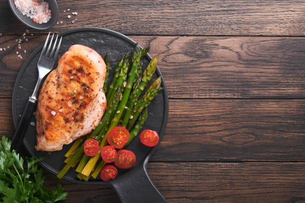 Chicken breast grilled with vegetables. Grilled chicken steak, asparagus and cherry tomatoes in black plate on wooden dark table background. Healthy diet lunch. Barbecue steak fried. Top view.