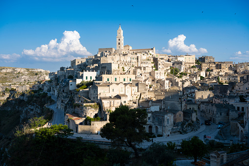 An idyllic cityscape of the old town of Matera, known worldwide as the 'Sassi di Matera' (Matera's Stones Hills). In the image the Sasso Caveoso hill, seen from a belvedere. The ancient city of Matera, in the region of Basilicata, in southern Italy, is one of the oldest urban settlements in the world, with a human presence that dates back to more than 9,000 years ago, in the Paleolithic period. The Matera settlement stands on two rocky limestone hills called 'Sassi' (Sasso Caveoso and Sasso Barisano), where the first human communities lived in the caves of the area. The rock cavities have served over the centuries as a primitive dwelling, foundations and material for the construction of houses, roads and beautiful churches, making Matera a unique city in the world. In 1993 the Sassi of Matera were declared a World Heritage Site by Unesco. Super wide angle image in high definition format.